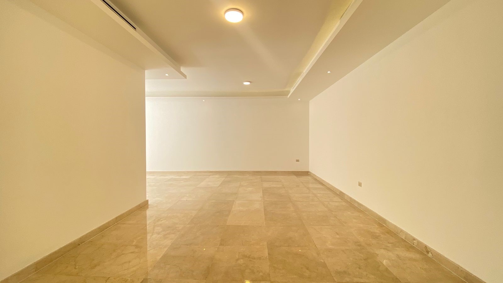 56e109fa-7d9c-46b0-bb98-f8c829634d4a Long empty rectangular room with beige marble tile floor and white walls, lit by recessed ceiling lights