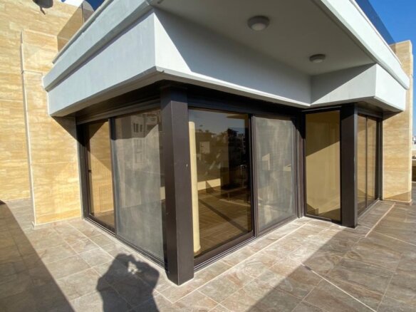 Corner of a modern storefront with large glass doors and beige stone walls on a tiled terrace sunlit exterior