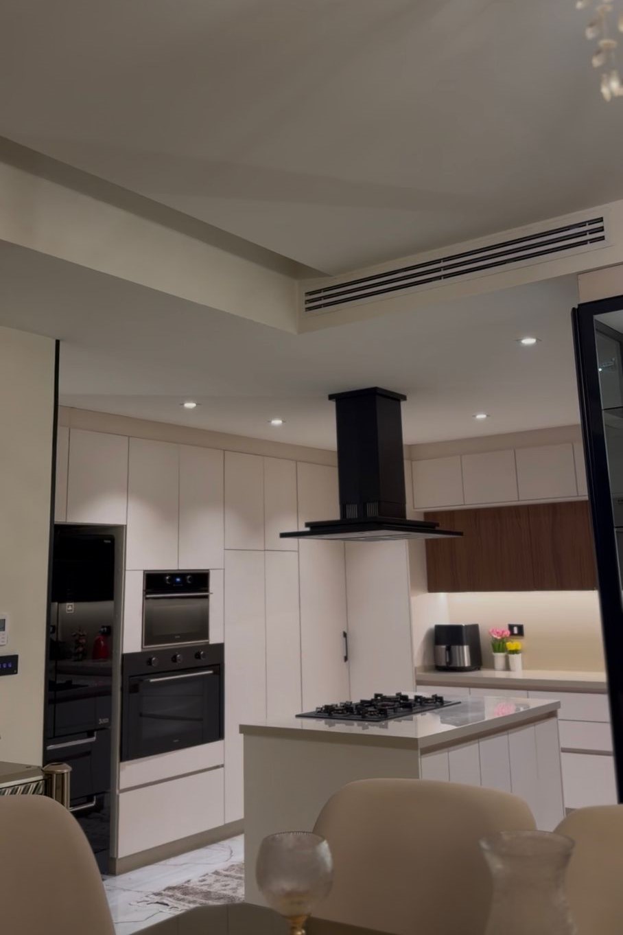 6476412a-b195-4121-a658-160ab40abca6 Modern white kitchen with island, gas cooktop, and black range hood above the stove.