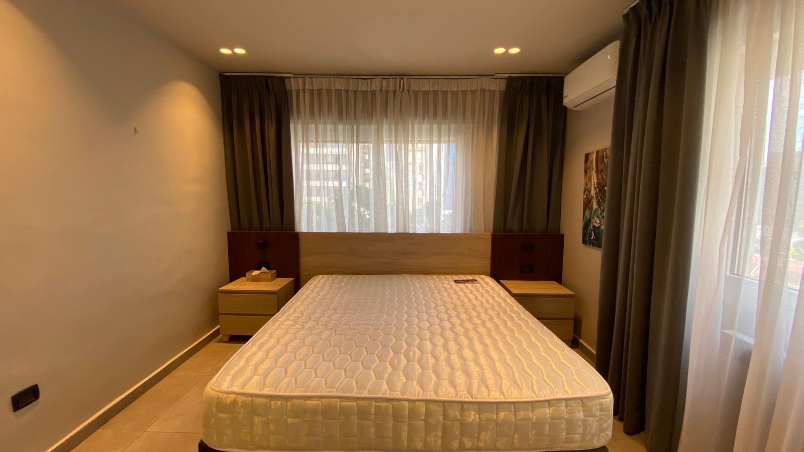 686c0c13-2e0a-464e-b8be-dae2638c3365 A modern bedroom with a large bed, two wooden nightstands, and a window framed by dark and sheer curtains.