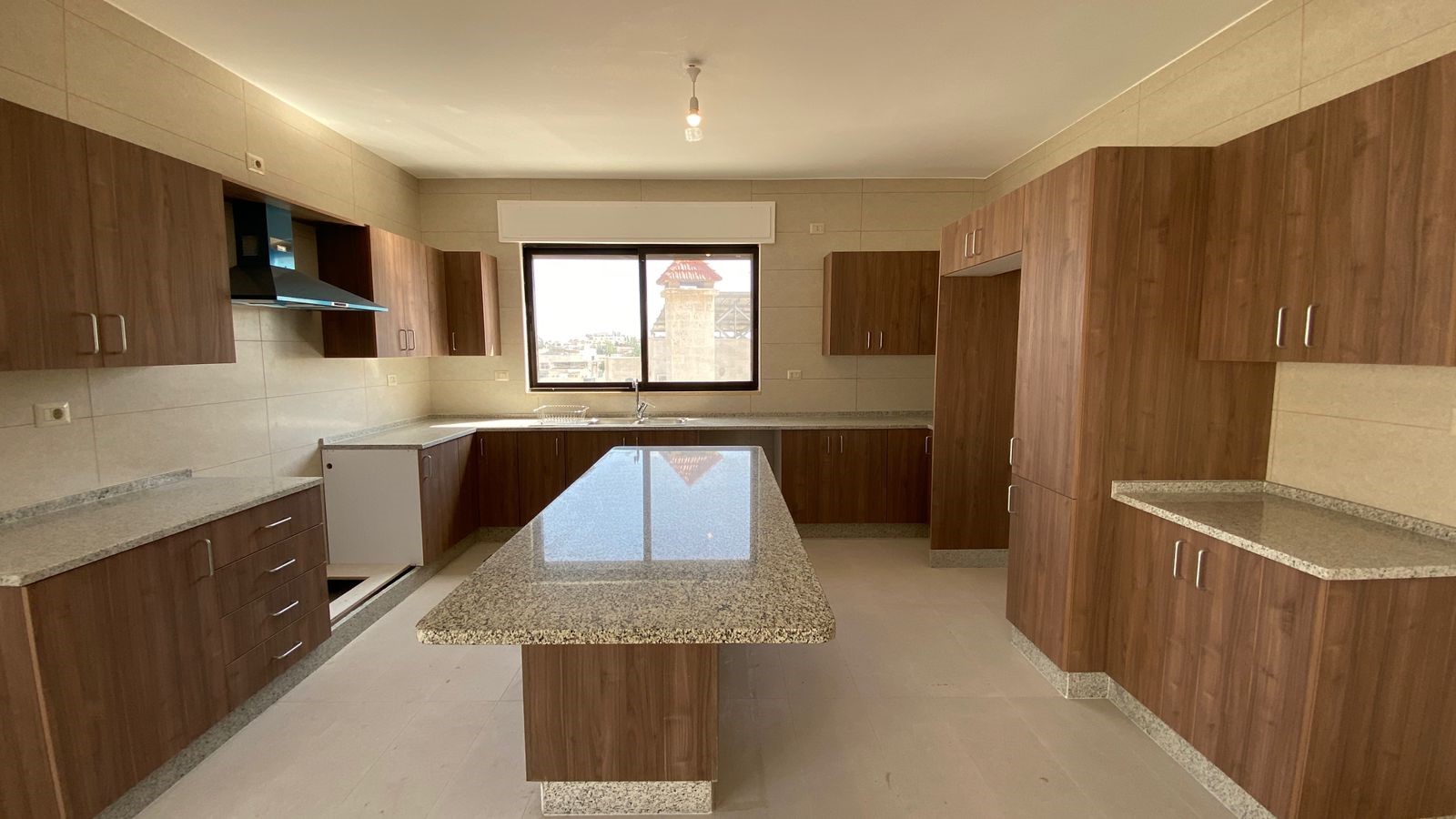 6b7b3393-1236-4b68-a0bb-a773c7f57f1f Modern kitchen with granite island and wooden cabinets, stainless sink under a window and a range hood on the left wall