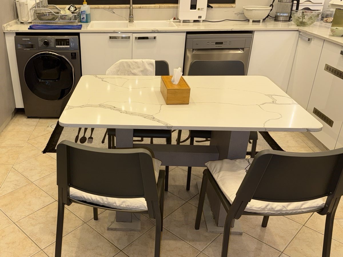6d1936e2-13ca-4464-bb23-c14b0c040112 White marble dining table with four gray folding chairs and a wooden tissue box in the center.