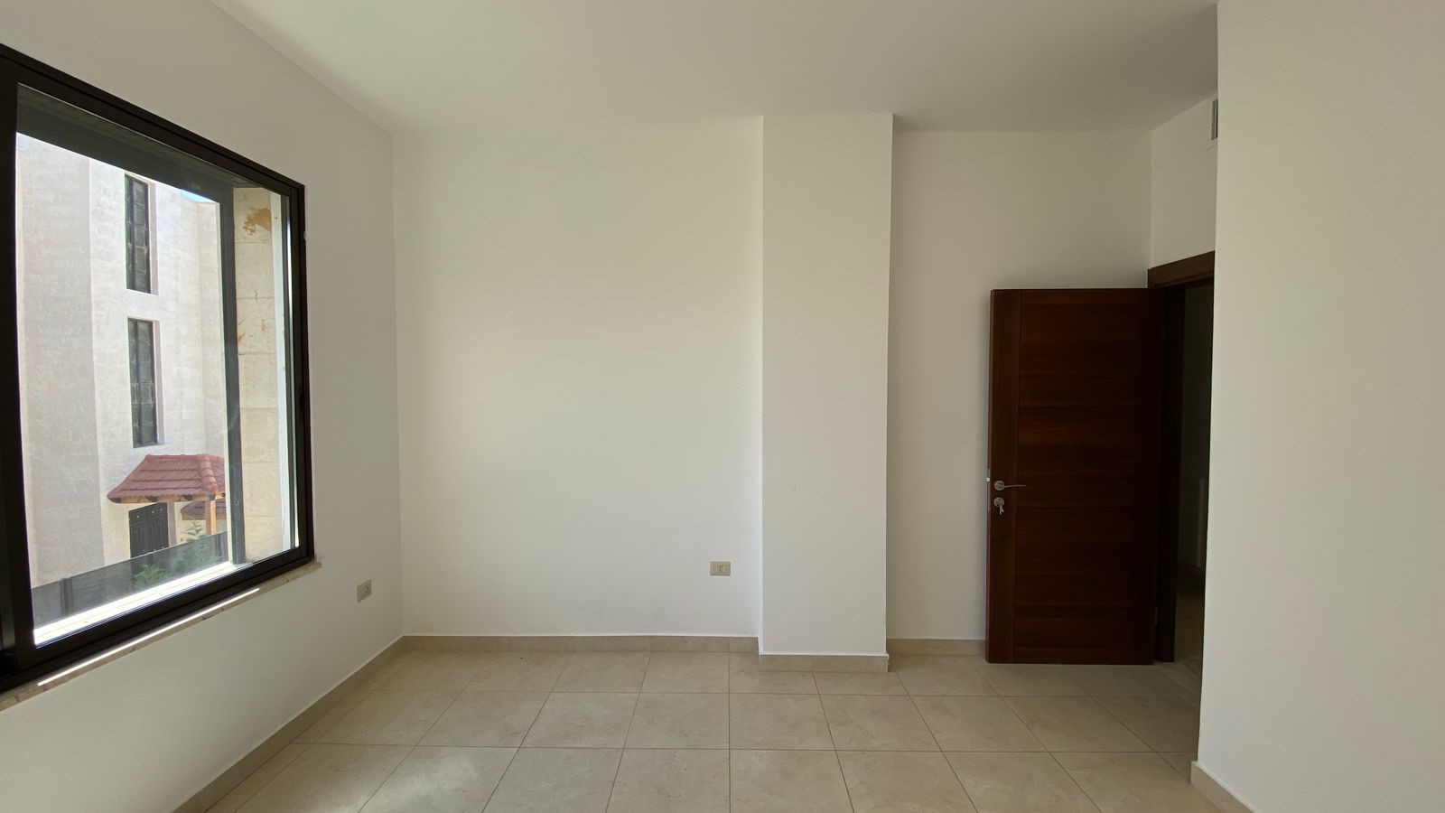 6e5b208a-4855-4477-b61b-514c847b447c Empty bright room with a large left-side window and an open brown wooden door to the right.