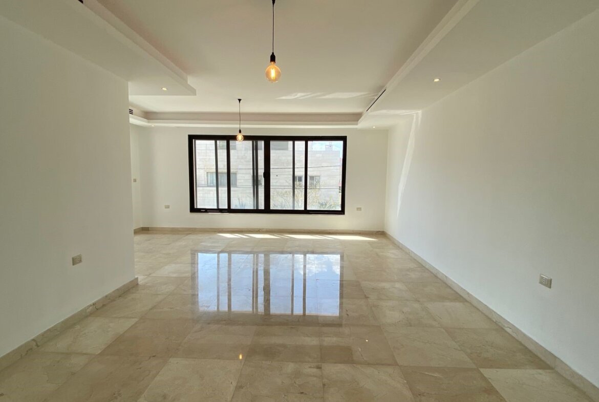Empty modern living room with a large black-framed window, white walls, and glossy beige marble floors.