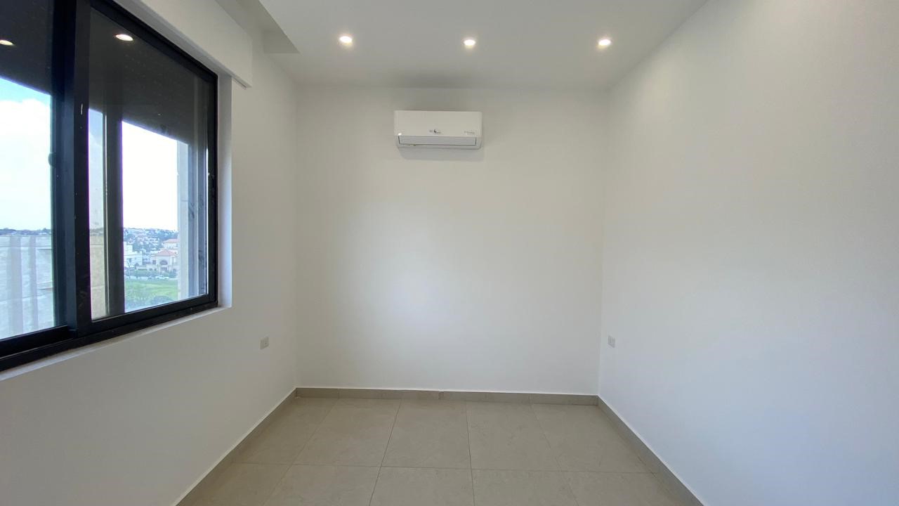 778f4599-3e4e-4601-b425-28d8a0825364 1 Empty white room with a large left window, tiled floor, ceiling lights, and a wall-mounted air conditioner.