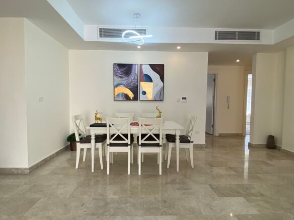 Bright dining area with a white table and six white chairs, two-panel abstract art, and gold deer figurines under a modern loop chandelier.