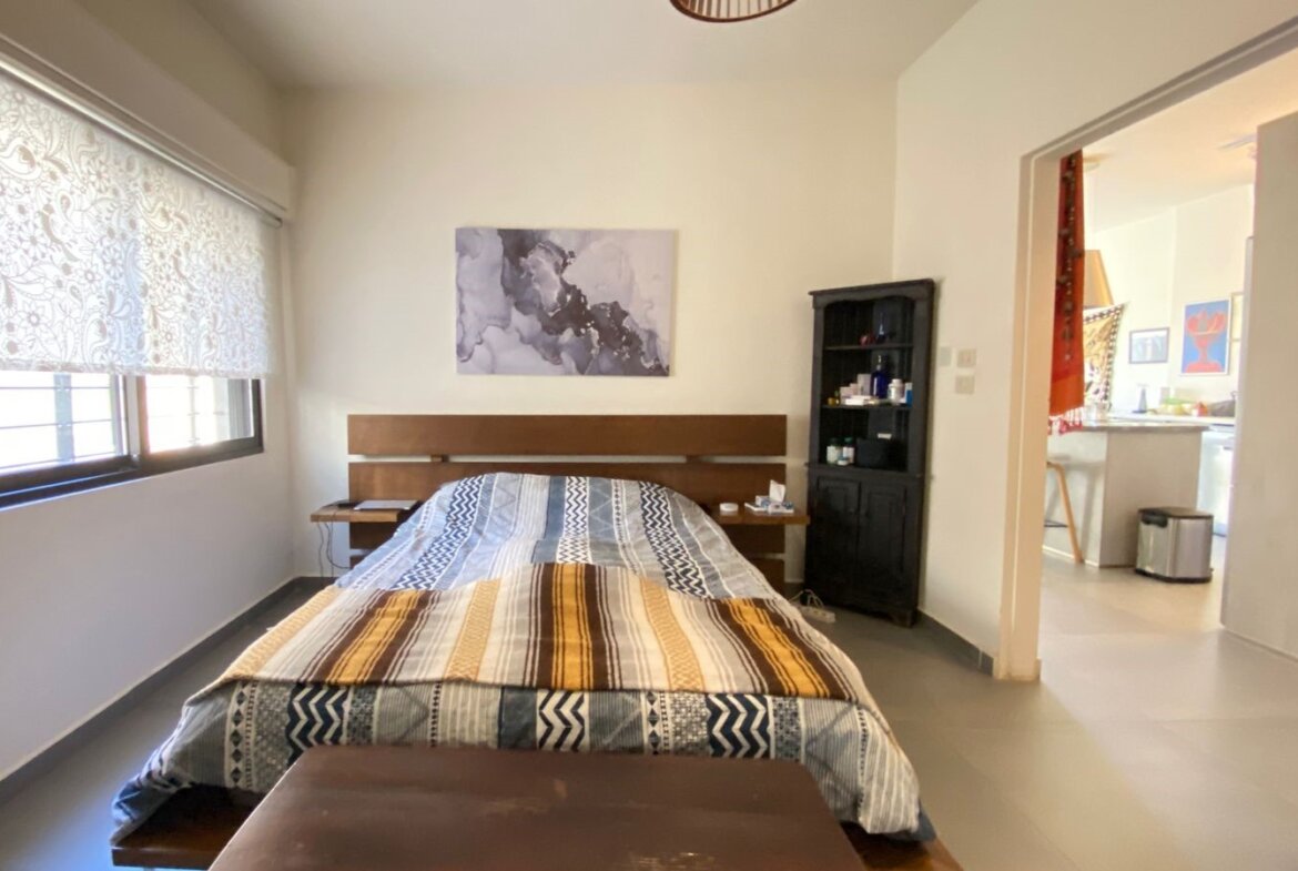 Bedroom with a low wooden bed, two small nightstands, a striped quilt, and a black cabinet beside the headboard.