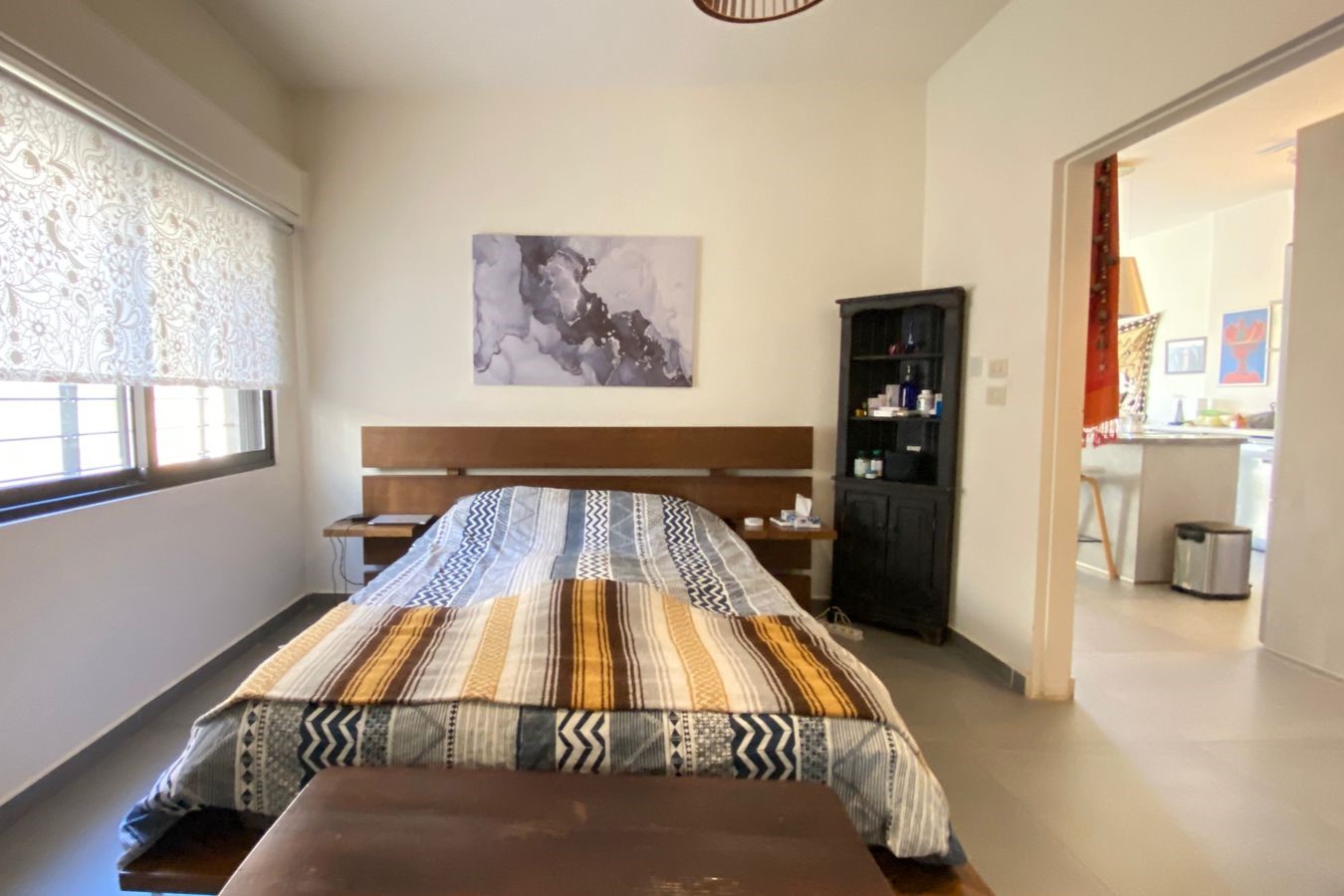 Bedroom with a low wooden bed, two small nightstands, a striped quilt, and a black cabinet beside the headboard.