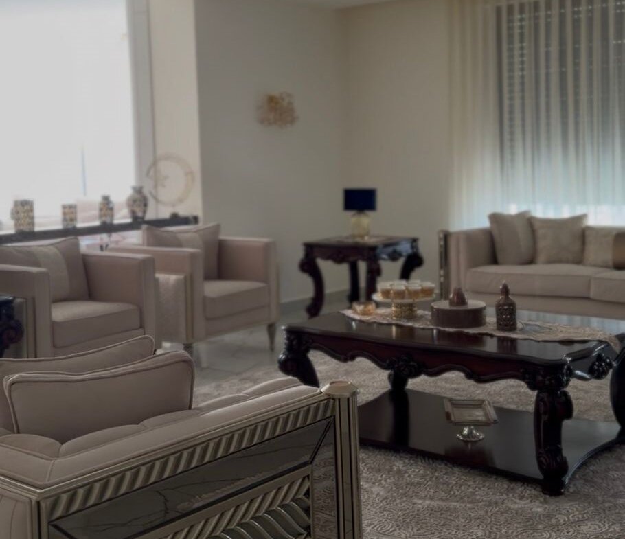 Luxurious living room with cream tufted seating, ornate dark wood coffee table, and a crystal chandelier.