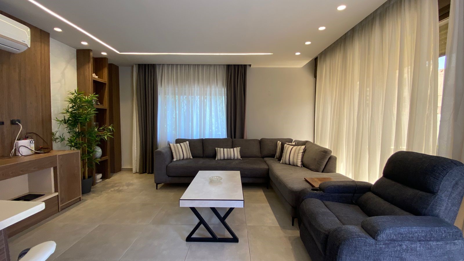 80a5ffd6-763c-4313-814f-129cb467855c Modern living room with a gray sectional sofa, matching chairs, and a white marble coffee table on a tiled floor.