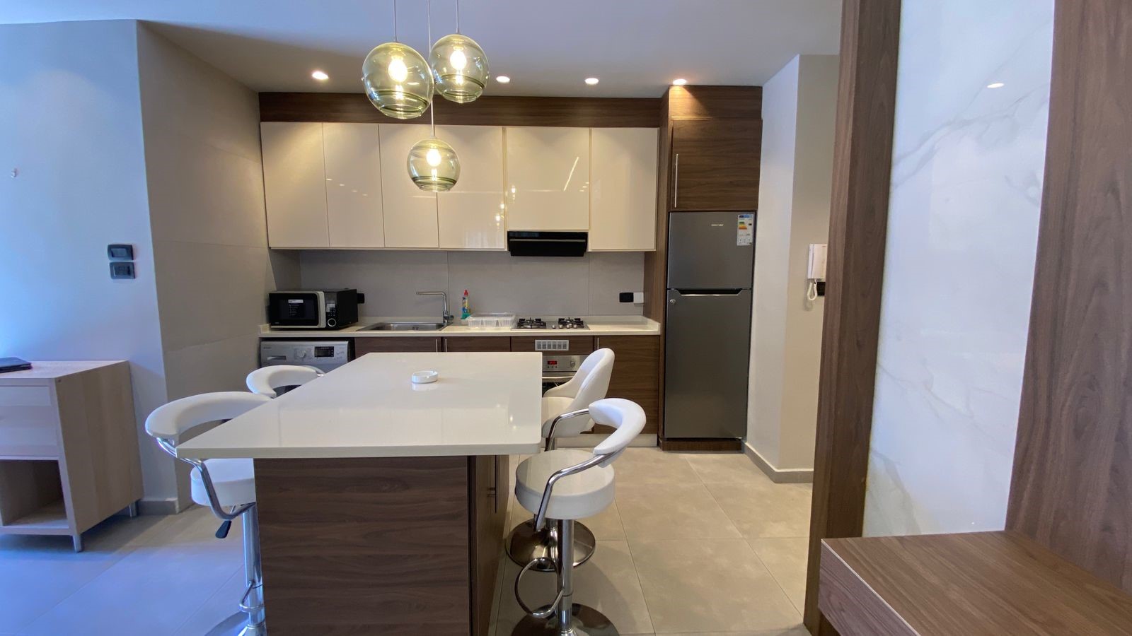 80f1bdfd-5790-4864-b93b-de572bc8c46c Modern kitchen with white upper cabinets, wooden lower cabinets, and a white island with bar stools.