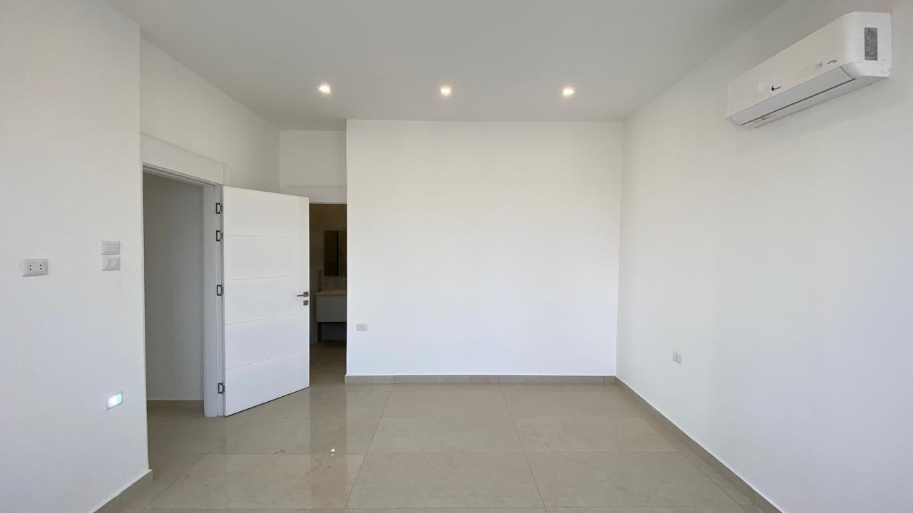 83d1dcfe-8176-42be-ad34-3f60e78aa623 Empty white-walled room with glossy tile floor, open door to adjacent space, and a wall-mounted AC unit on the right.