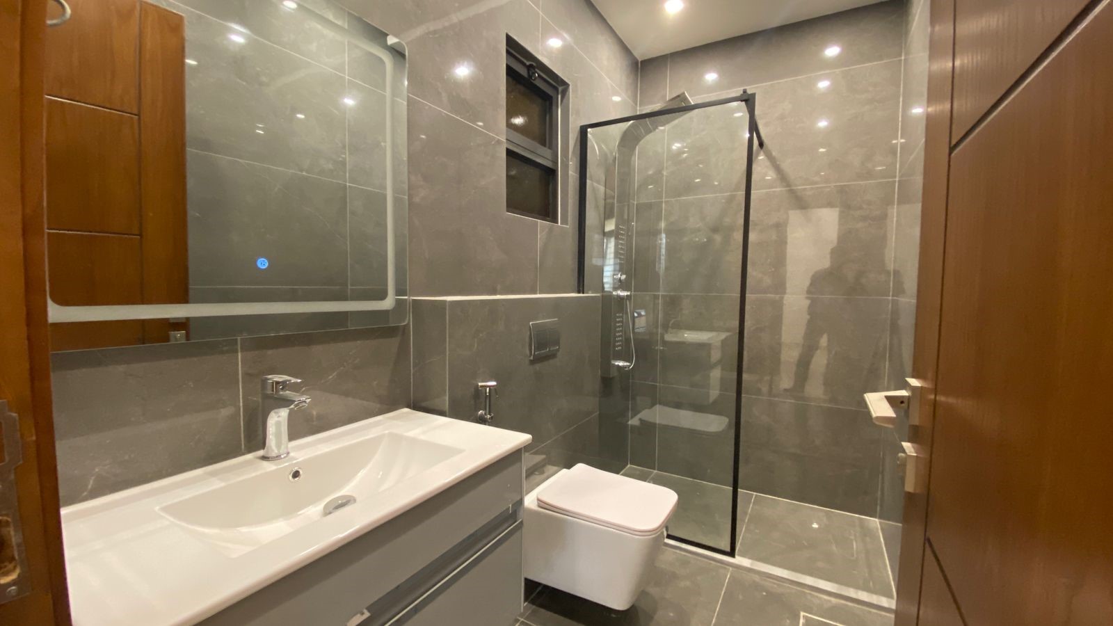 85110197-5c27-41c7-87c2-1558407ab7b2 Modern gray-tiled bathroom with a white sink, wall-mounted faucet, large mirror, and glass shower enclosure.