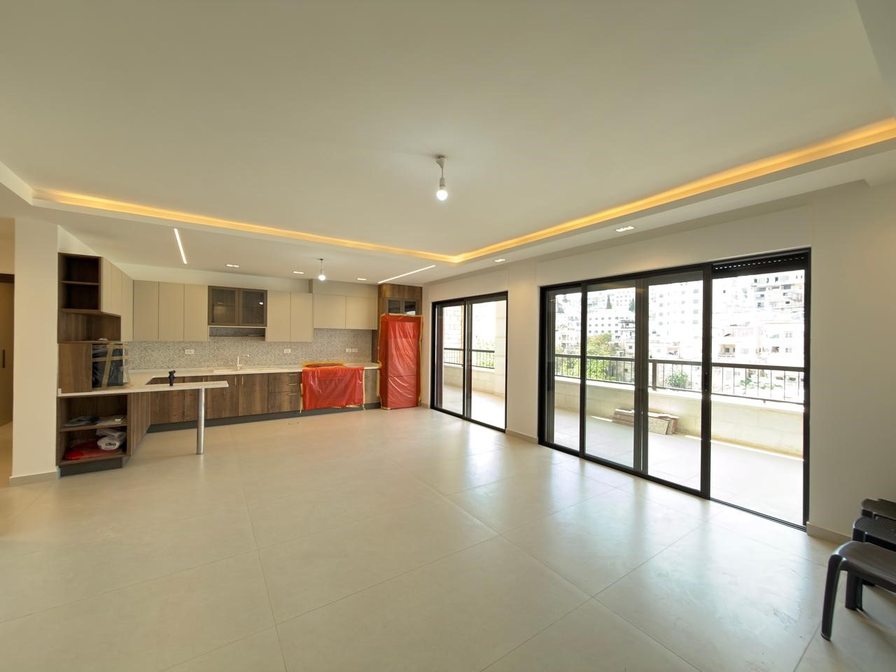 8729b666-08ba-4610-9d11-b5edd47197ea Open-plan kitchen and living area with tiled floors, modern cabinetry, and large sliding glass doors to a balcony facing an urban view.