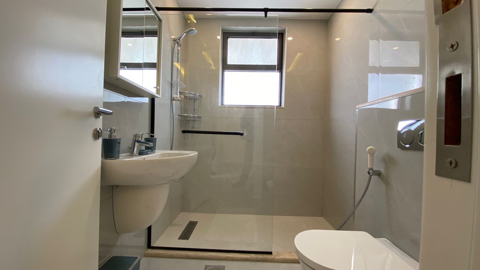 8a5dee9f-ef41-43a3-824a-4dac541e2ce7 Modern bathroom with a glass-enclosed shower, wall-mounted sink, and a windowsill light behind the door edge.