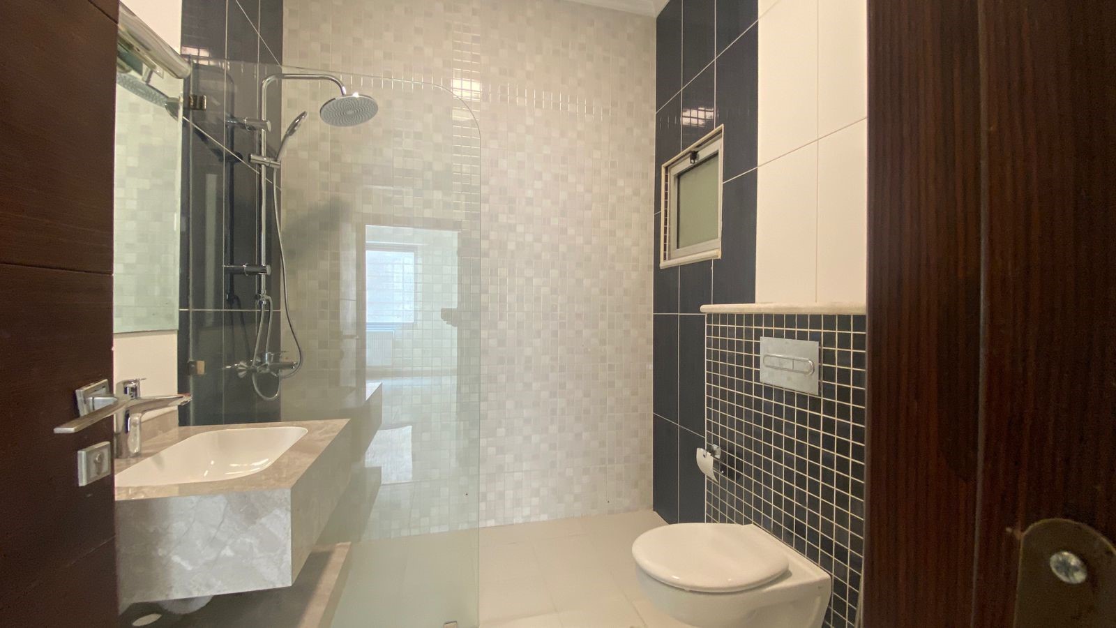 8b14ce92-20d5-4c3d-adb2-cf6cf40e96da Modern bathroom with glass shower enclosure, wall tiling, sink, and wall-hung toilet.