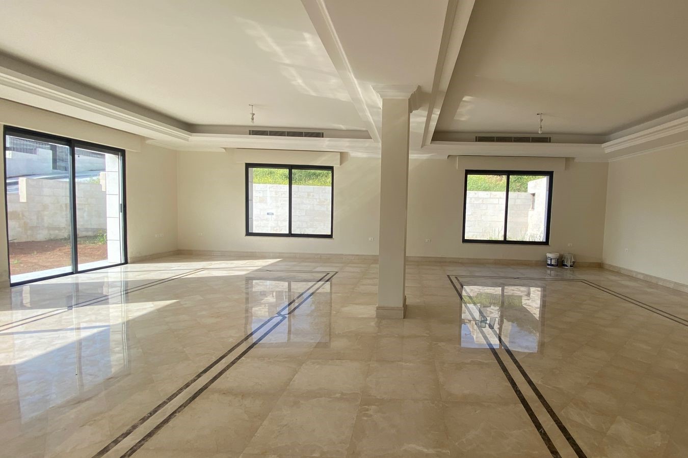 8d99e8bb-8b39-4d10-9726-695b7a8e021b Spacious empty living room with polished marble floors, large windows, and sliding glass doors to the outside.