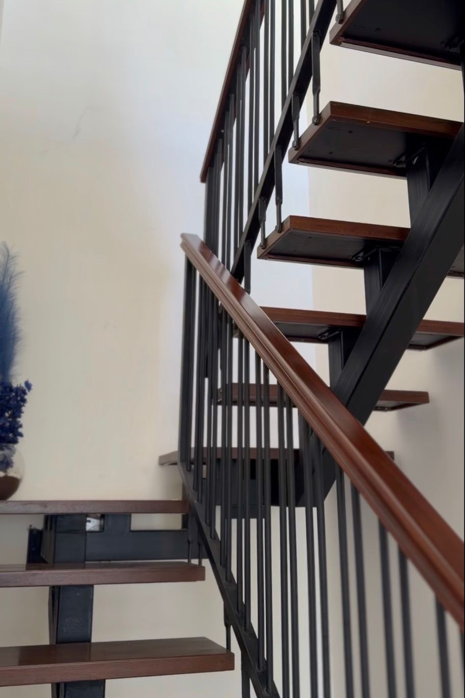 914791de-8845-4388-b99d-4397e0491e04 Modern open-riser staircase with a black metal frame and wooden treads, railing along one side in a bright interior.