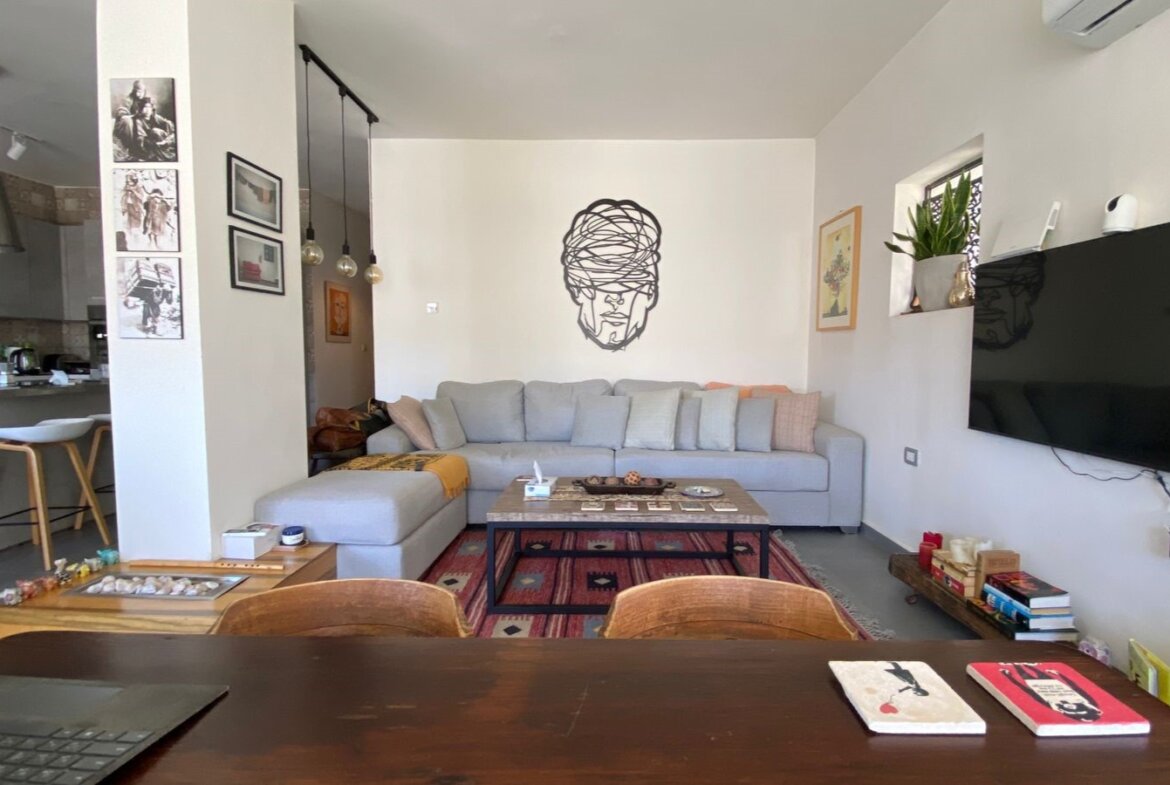 Living room with a gray sectional sofa, wall art of a tangled-head silhouette, and a coffee table on a red rug.