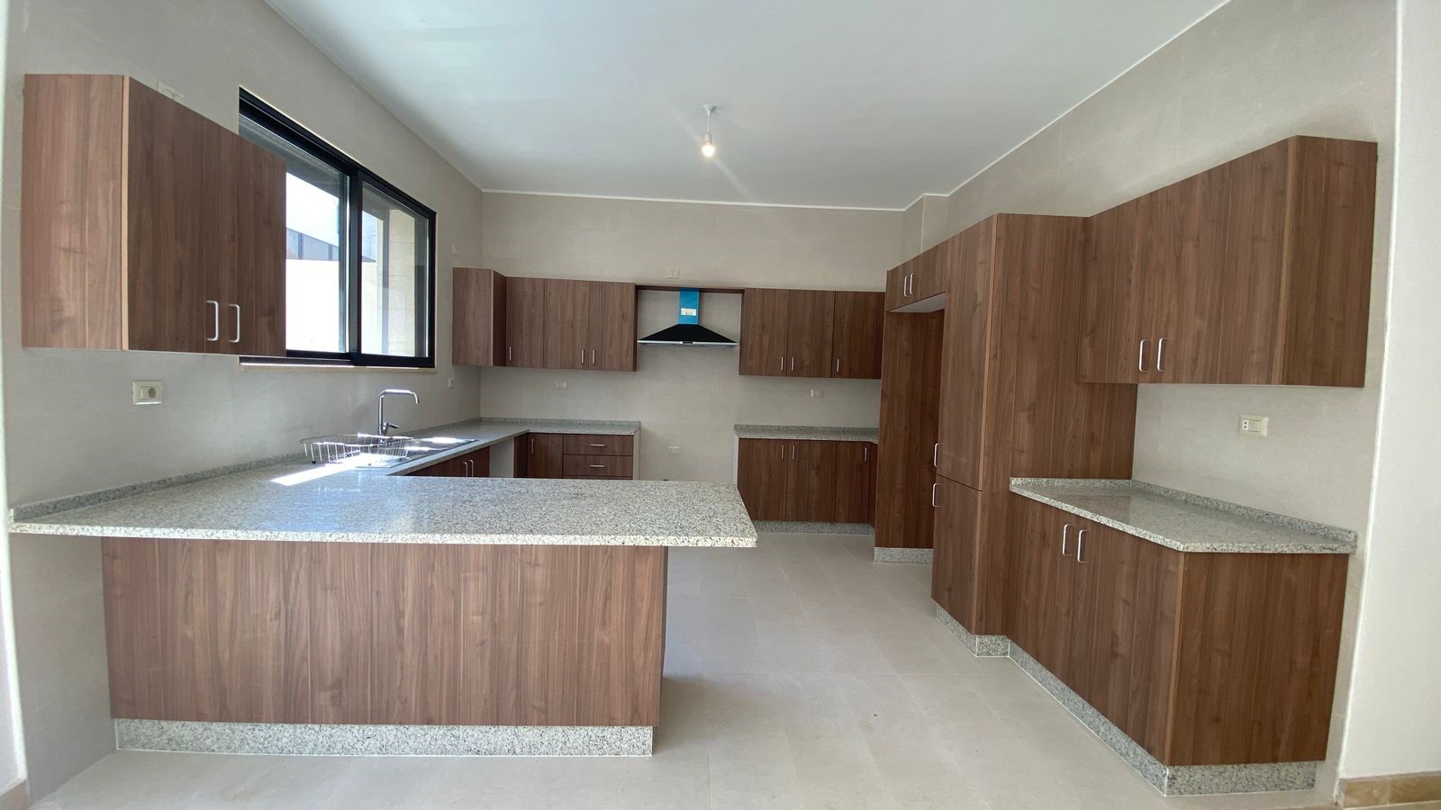 991feff3-95ca-4cb2-9b2f-96eca657e890 Modern L-shaped kitchen with wood grain cabinets, granite countertops, and a central island; stainless sink beneath a large window on the left.