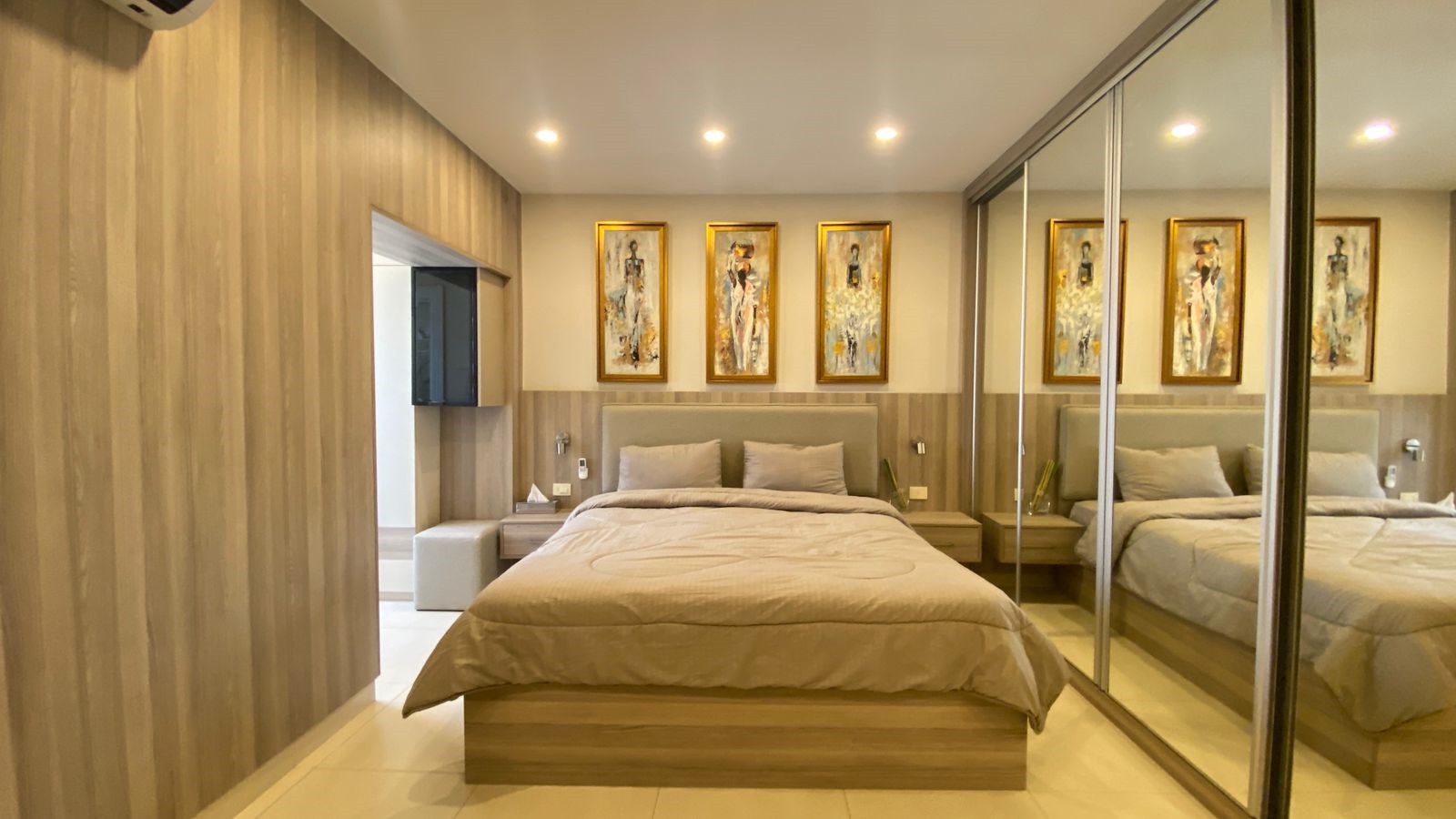 9be3a482-c40c-48c1-9e9b-4000c5f0a071 Modern hotel bedroom with a king-size bed, beige bedding, and four framed paintings above the headboard.