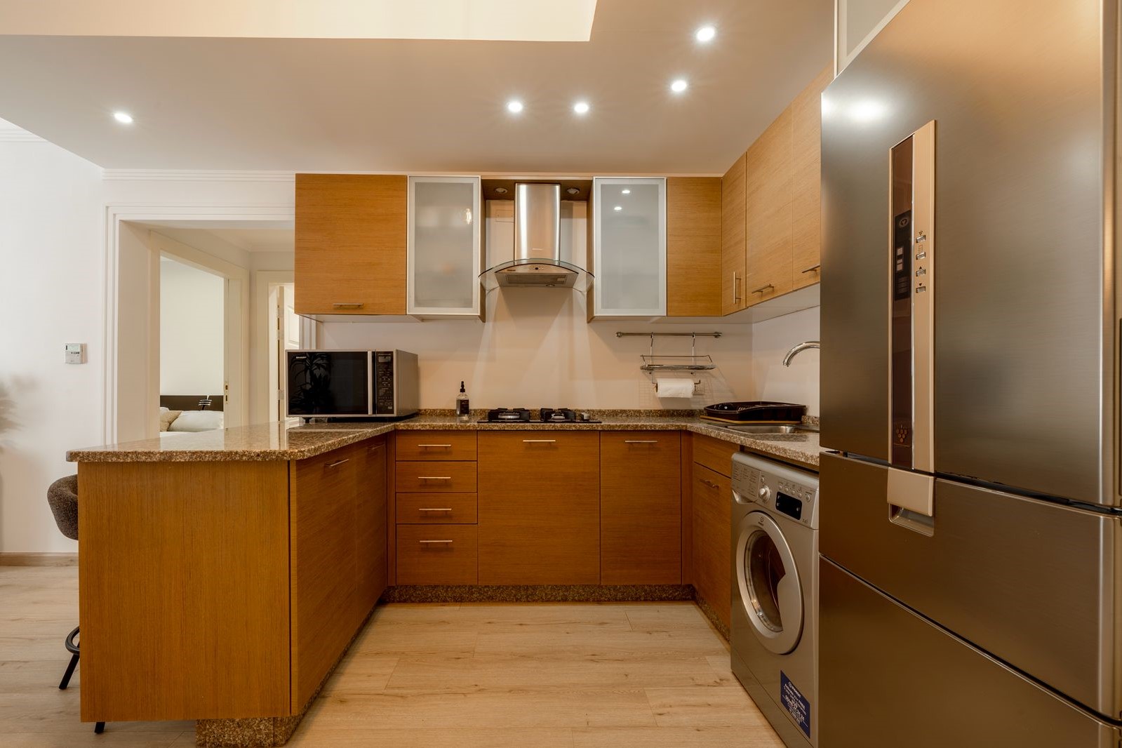 9d927a46-73a4-4e7d-97eb-832011deeb71 Modern L-shaped kitchen with wooden cabinets, granite countertops, and stainless steel appliances.