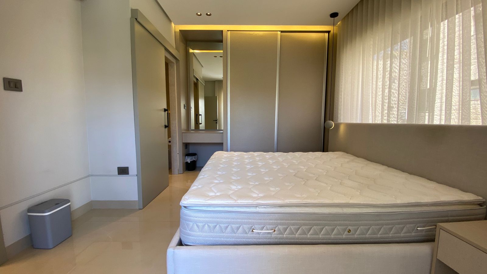 WhatsApp Image 2026-04-21 at 122948 PM 2 Hotel bedroom with a large mattress on a platform bed, sliding wardrobe, and sheer curtains in neutral tones