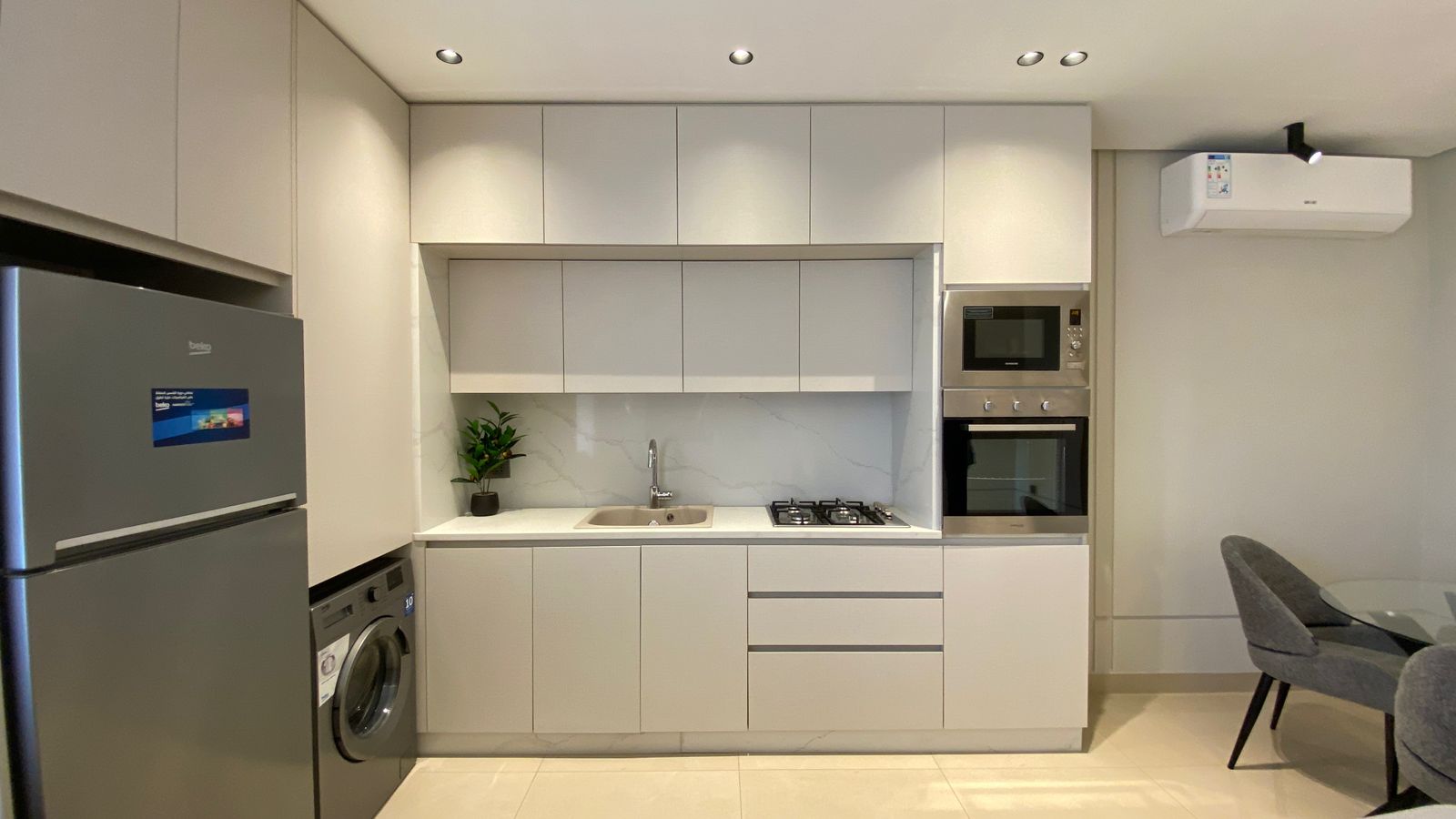 WhatsApp Image 2026-04-21 at 122948 PM Modern gray kitchen with built-in microwave and oven, gas stove, and a white marble backsplash above a sink.