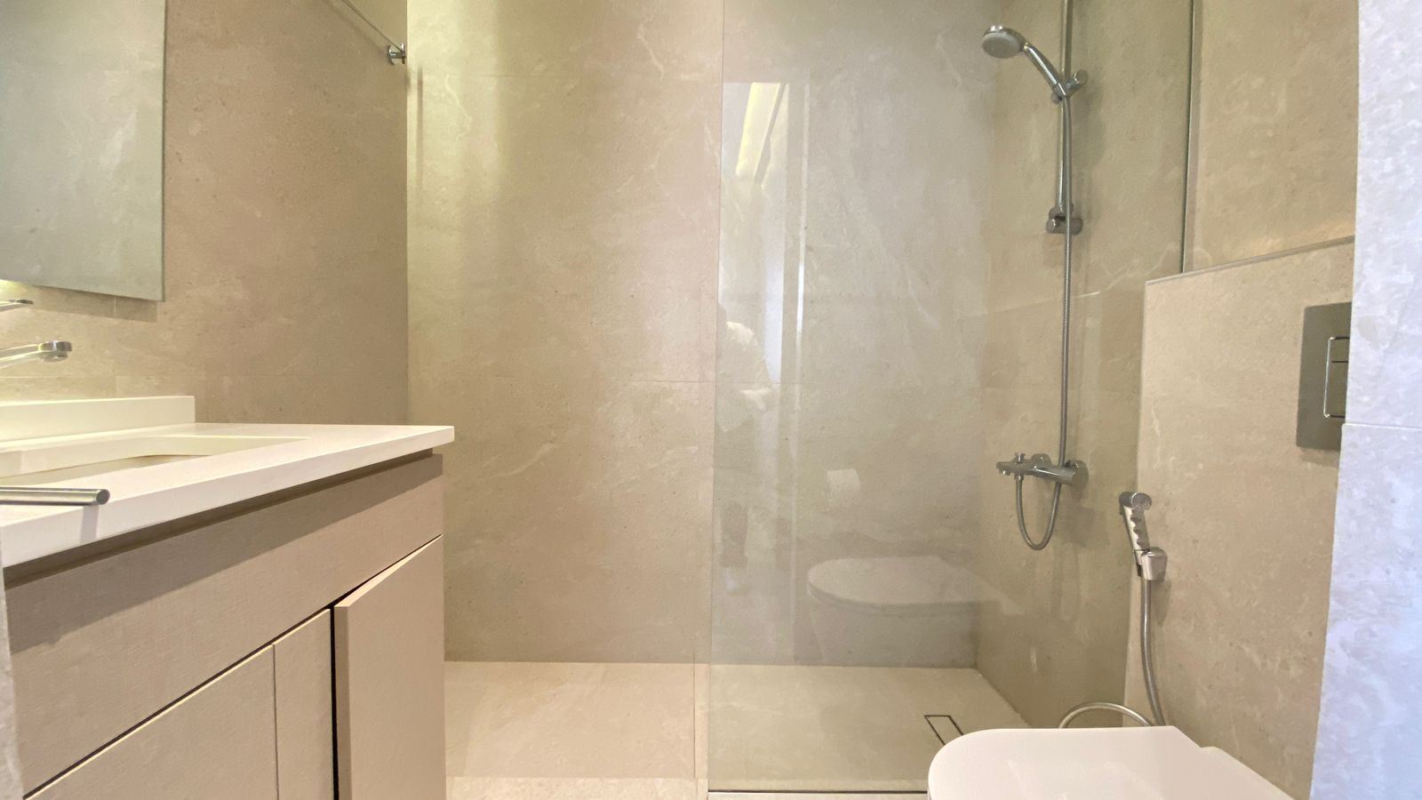 WhatsApp Image 2026-04-21 at 122949 PM 1 Modern bathroom with beige marble walls, glass-enclosed shower, and white vanity sink area.