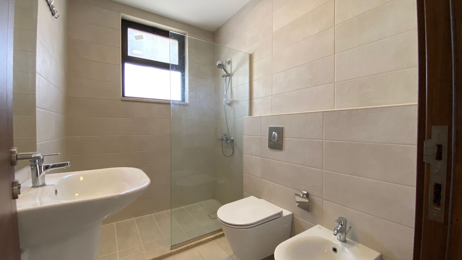 afe6cf9b-ab23-4e82-8503-01e3928b940f Modern bathroom with a glass-enclosed shower, wall-mounted toilet, bidet, and pedestal sink.