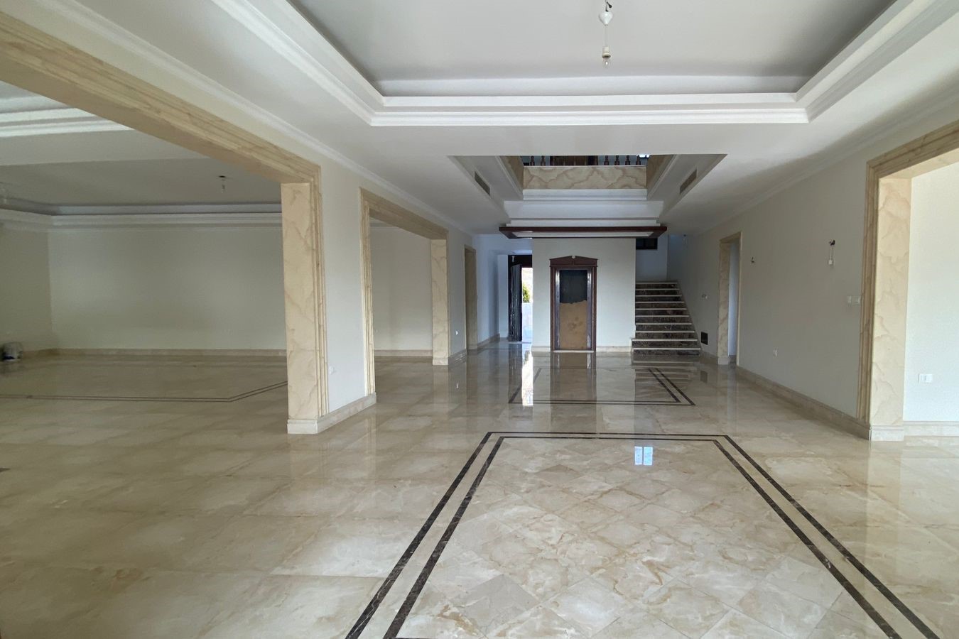 b9967e46-b0dc-411c-bfe2-f248c0c3d7b2 Spacious marble-floored lobby with beige columns and a staircase at the far end.