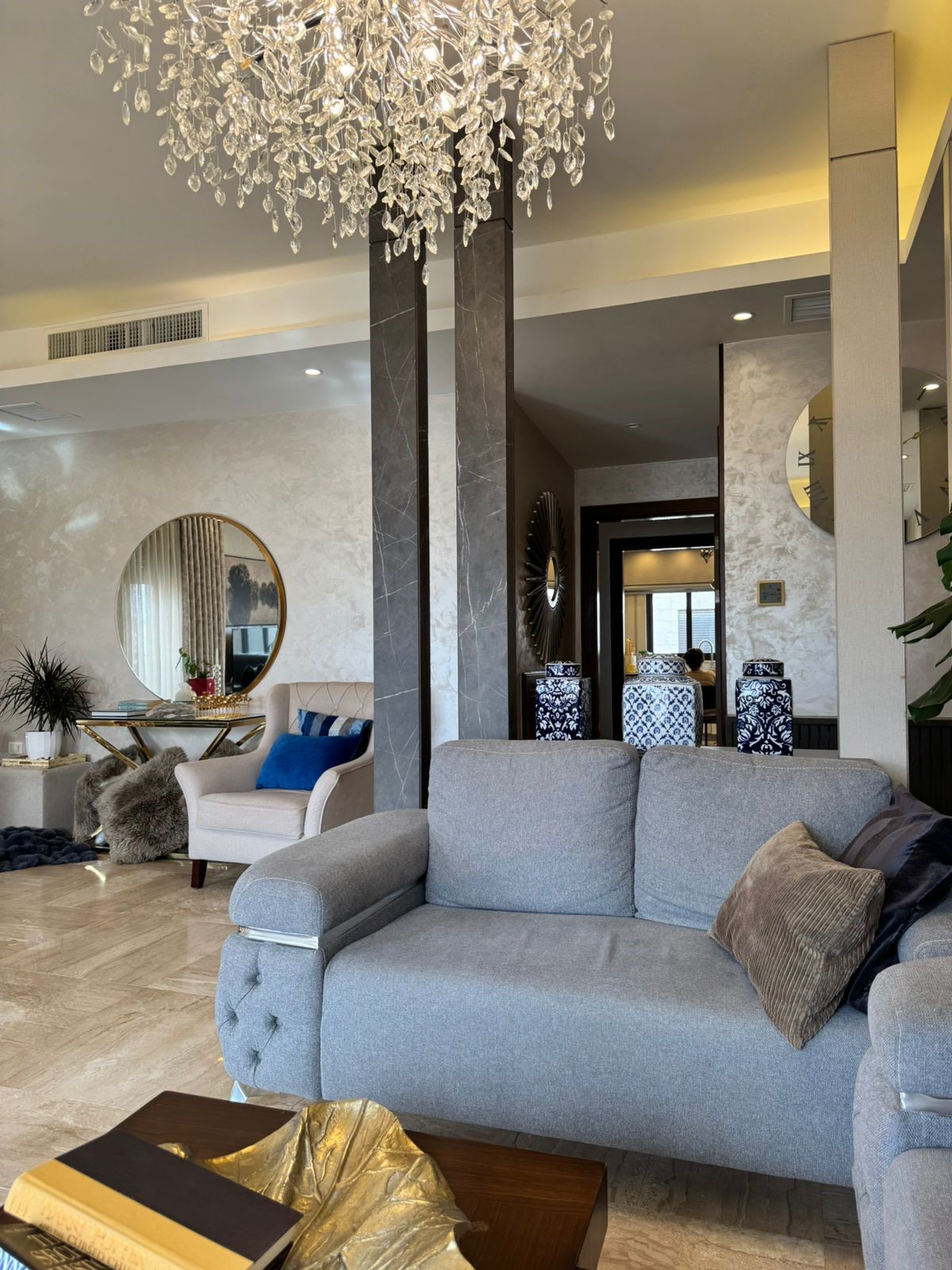 c3e6d848-233f-4e78-a165-70f58ed114e2 Luxurious living room lobby with a crystal chandelier, gray sofa, and decorative blue cushions.