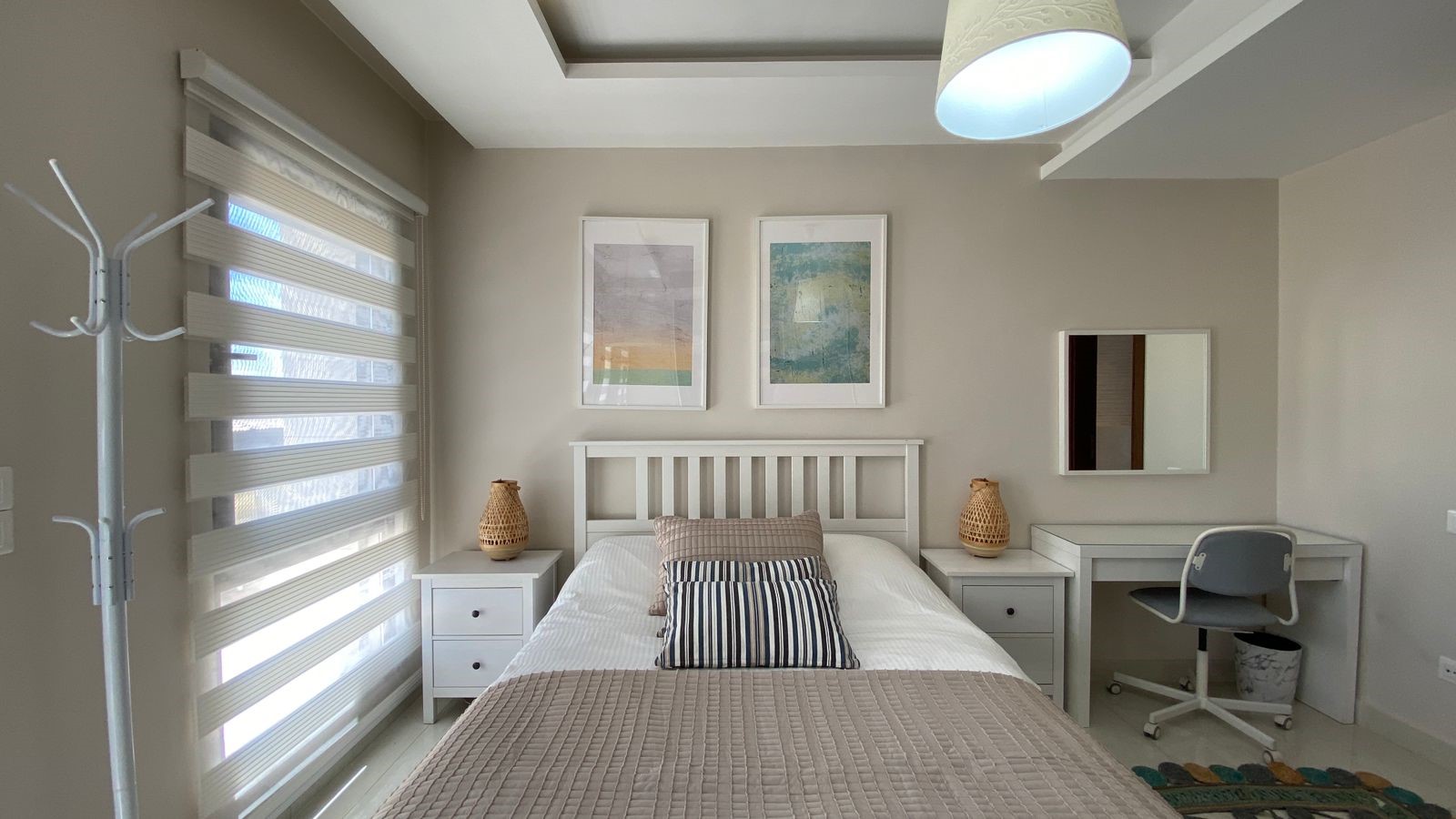 cd0f165b-8b52-48e0-abd7-efaa76680ca0 Bright bedroom with a white wooden bed, two nightstands, wicker lamps, and a desk with chair against the wall.