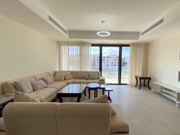 Bright living room with a beige sectional sofa, glass coffee tables, and large sliding doors to a balcony.