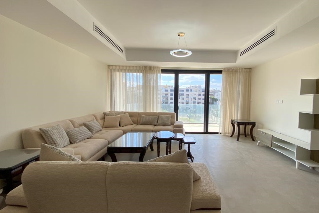 Bright living room with a beige sectional sofa, glass coffee tables, and large sliding doors to a balcony.