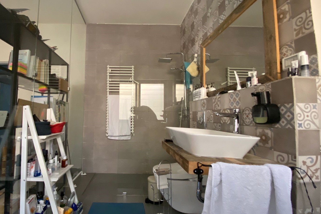 Modern bathroom with a white vessel sink on a wooden vanity, patterned tile wall, large mirror and glass shower enclosure.