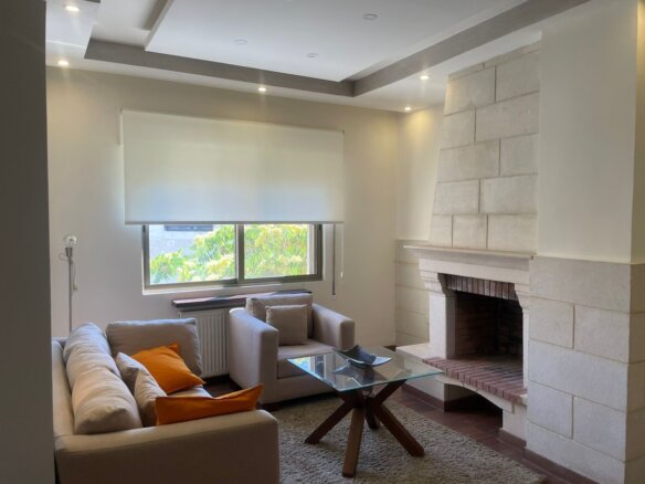 Modern living room with a stone fireplace, beige sofa, and orange cushions facing a glass coffee table.