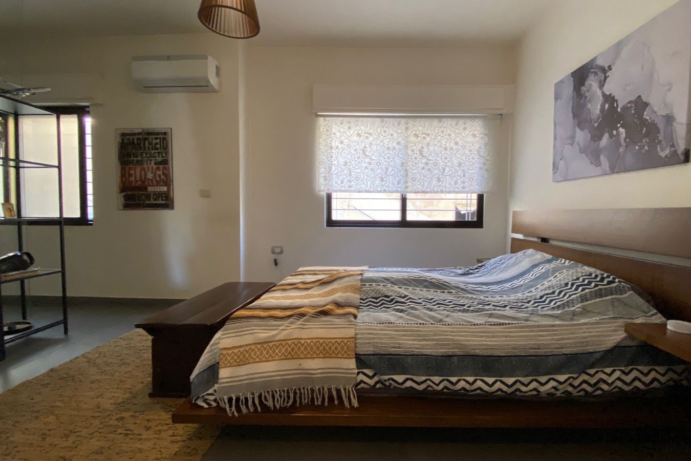 Bedroom with a low wooden platform bed, blue-gray striped duvet, and a beige woven throw at the foot.