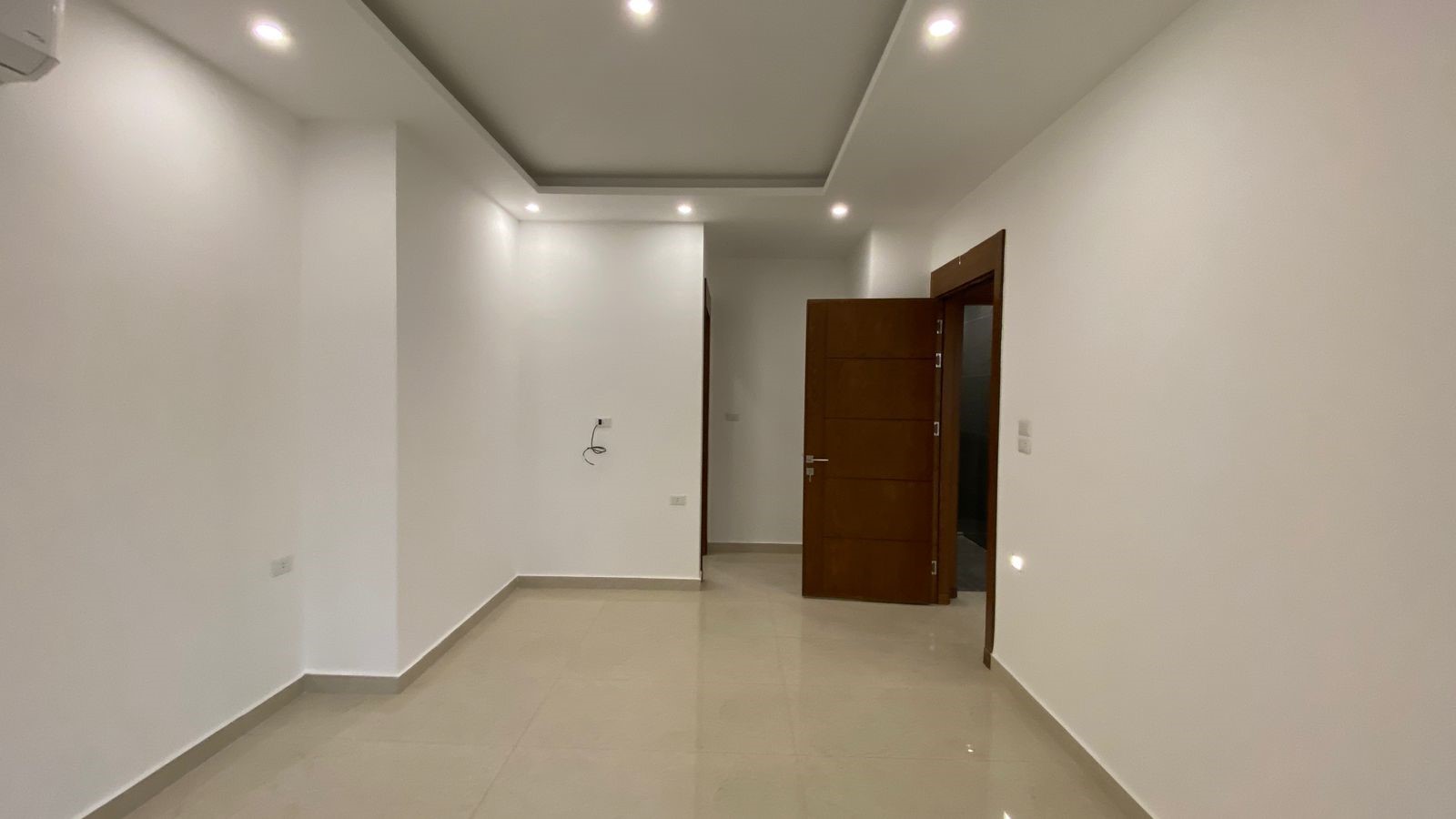 d46c04ca-ec09-461a-9af1-51bef3f6aa6f Empty modern hallway with white walls, beige tiled floor, and a partially open wooden door on the right.