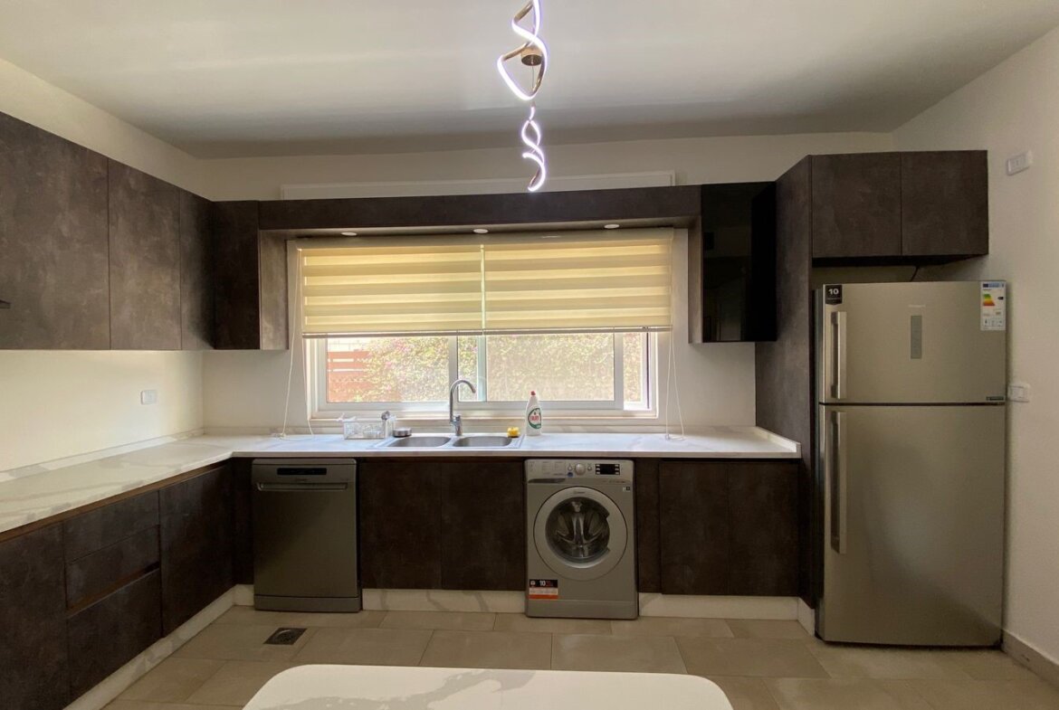 Modern L-shaped kitchen with dark wood cabinets, stainless steel appliances, and a window above the sink. A spiral pendant light hangs from the ceiling.