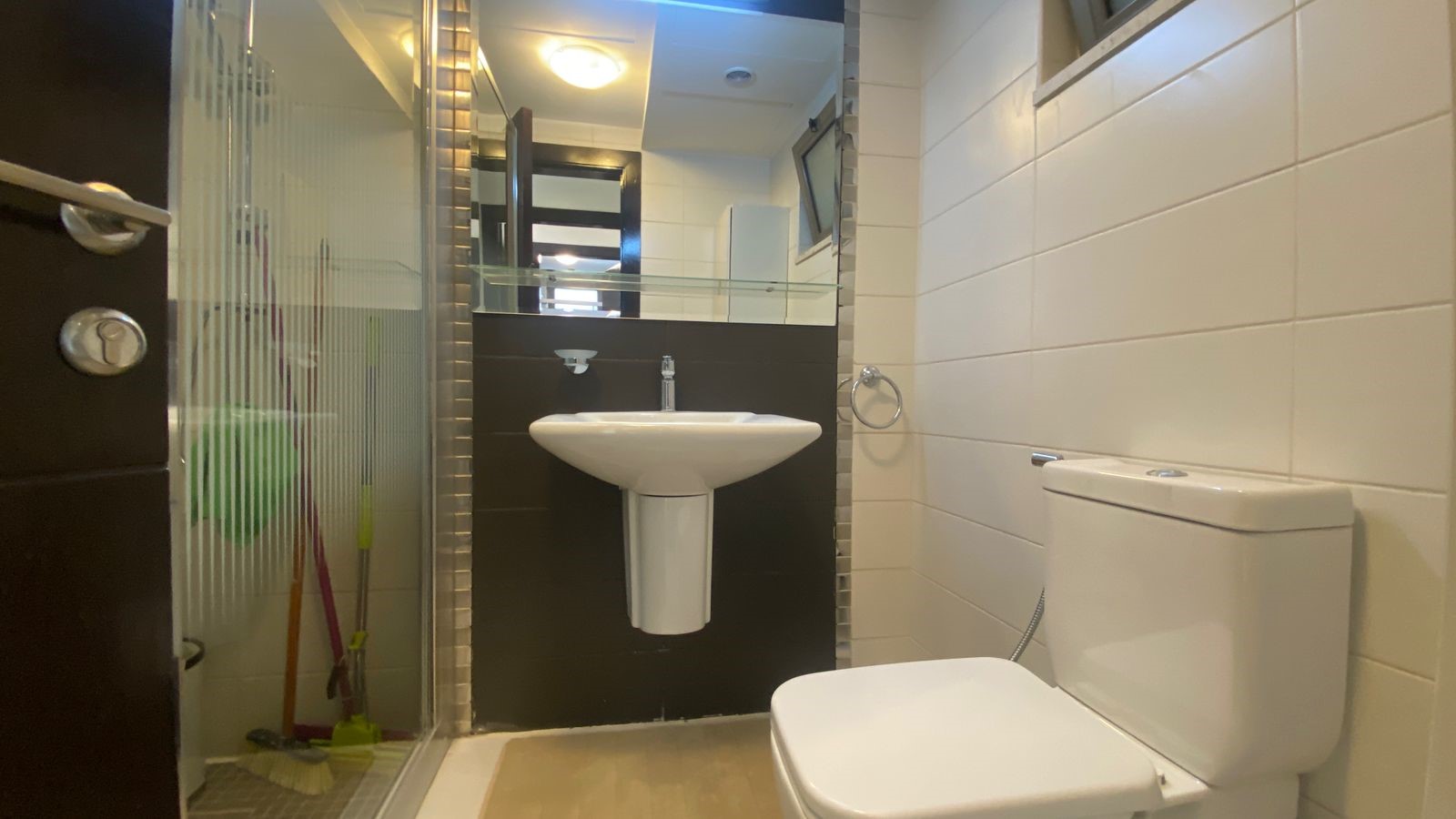 d85a207d-19fd-4fa6-aa44-117d95125471 Modern bathroom with pedestal sink, glass shower enclosure, and white toilet against a dark accent wall.