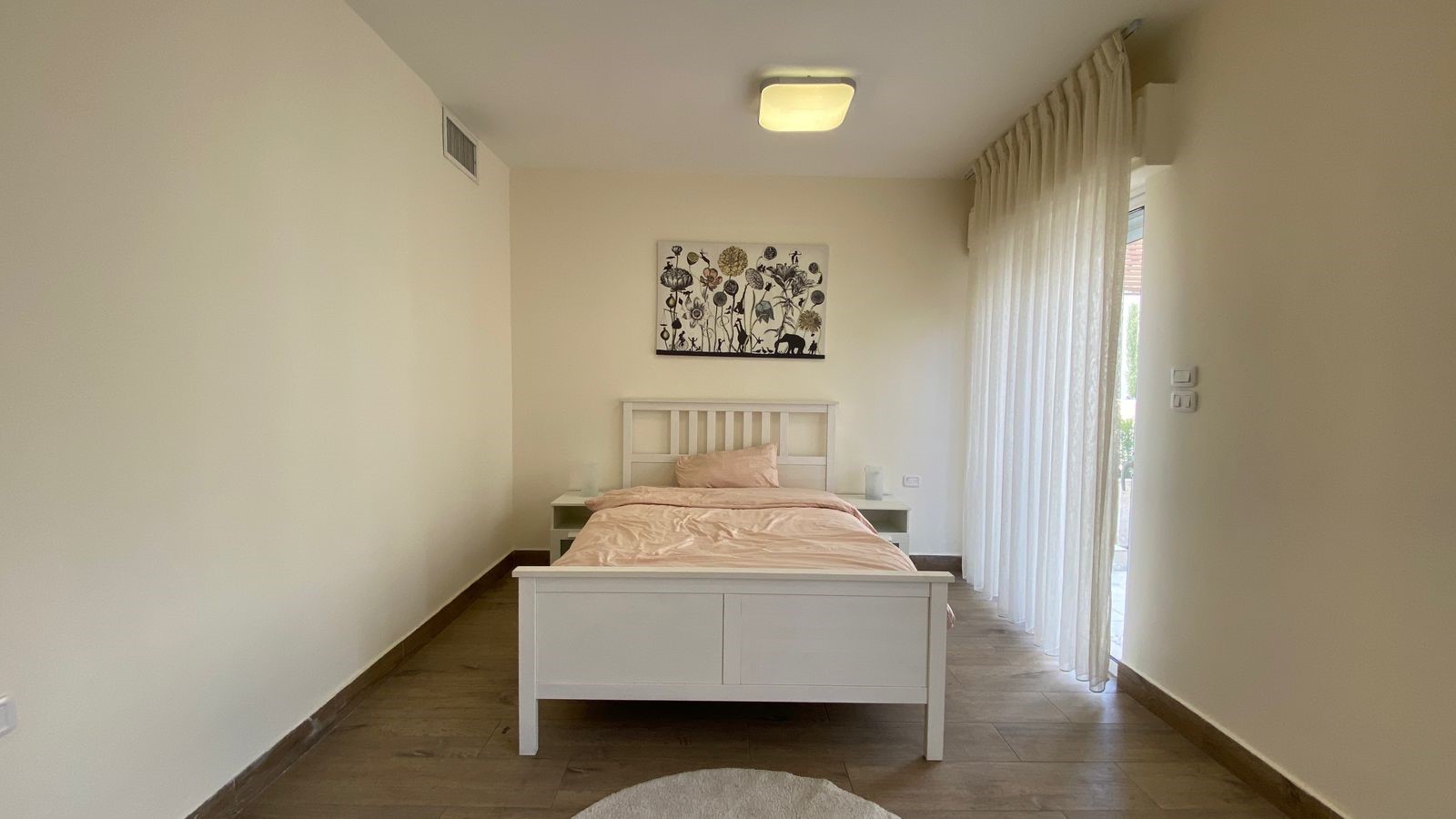 d990423b-995d-46cf-8cc4-aa1666233045 Minimalist white bedroom with a single bed, peach bedding, and two small white nightstands on either side; a black-and-white botanical artwork hangs above the headboard.