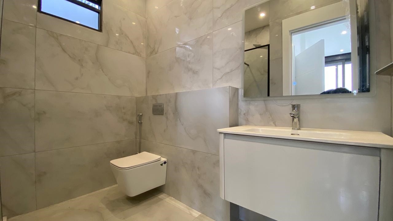 dbfc0d4b-a1f6-438a-9426-f89c923f6f05 Modern bathroom with marble walls and floor, a wall-mounted toilet, and a white vanity with sink.