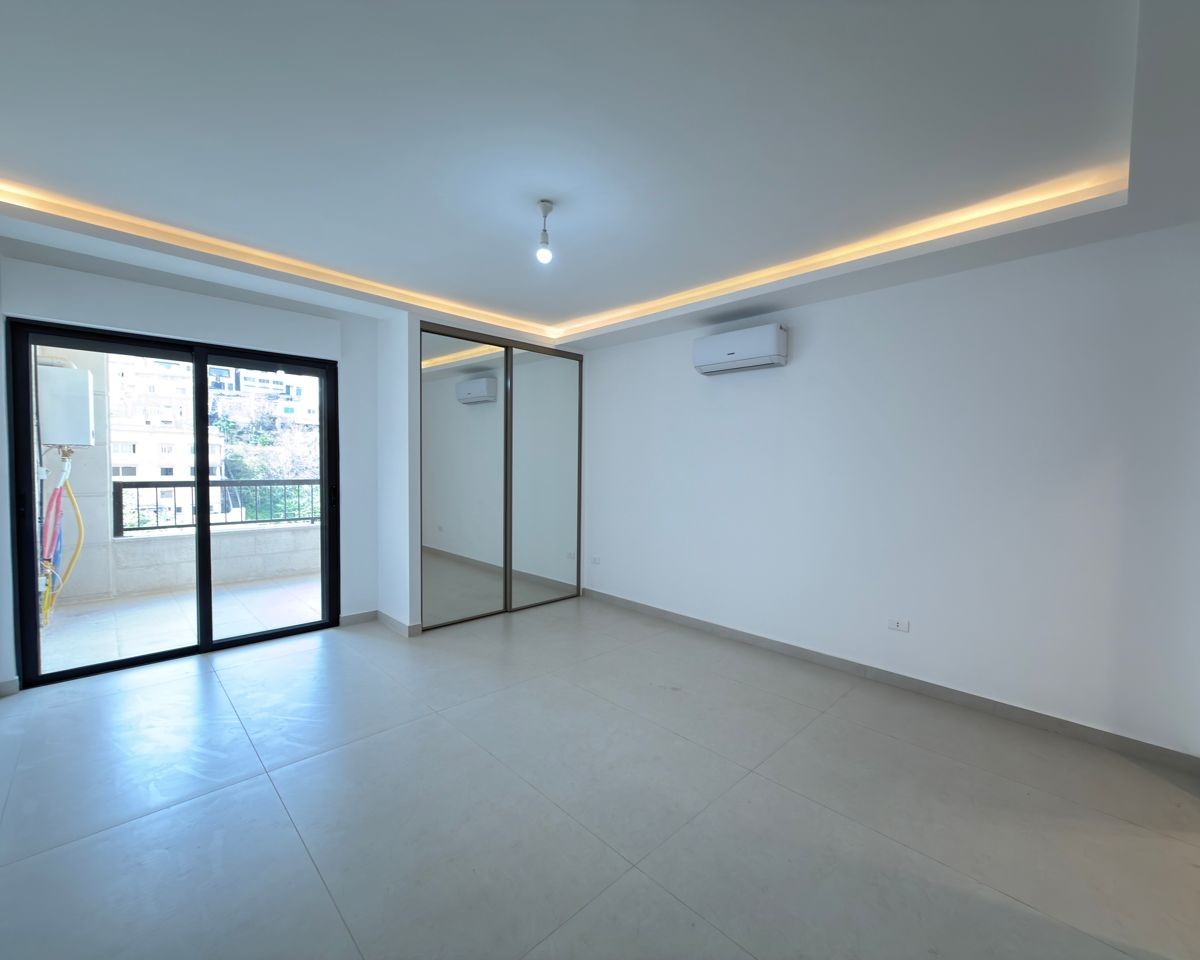 ea2a5c0c-d669-4eb0-84f4-81e62118fa79 Bright empty living room with sliding glass door to a balcony and a mirrored wardrobe on the wall/closet area at the back of the room.
