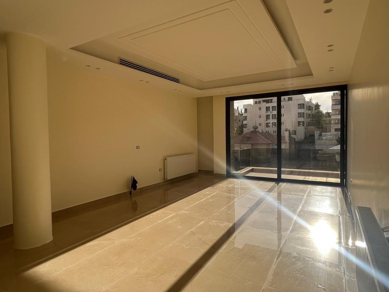 ea563d40-0019-47d7-86ef-609afa06964f Empty modern living room with a large glass sliding door to a balcony, polished beige tile floor, and a white support column on the left