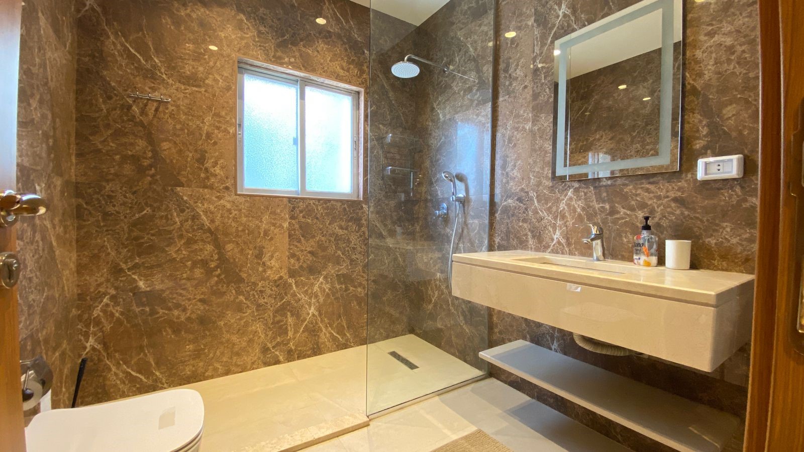 ef9488cc-419d-4e42-b28f-0911da601d1c Contemporary bathroom with brown marble walls, a glass-enclosed shower, and a wall-mounted sink with mirror.