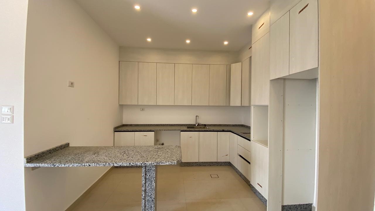 f150b543-8cee-4f7d-96de-4061ff195b8c Modern kitchen with white wood cabinets, gray granite countertops, and an island countertop in the foreground