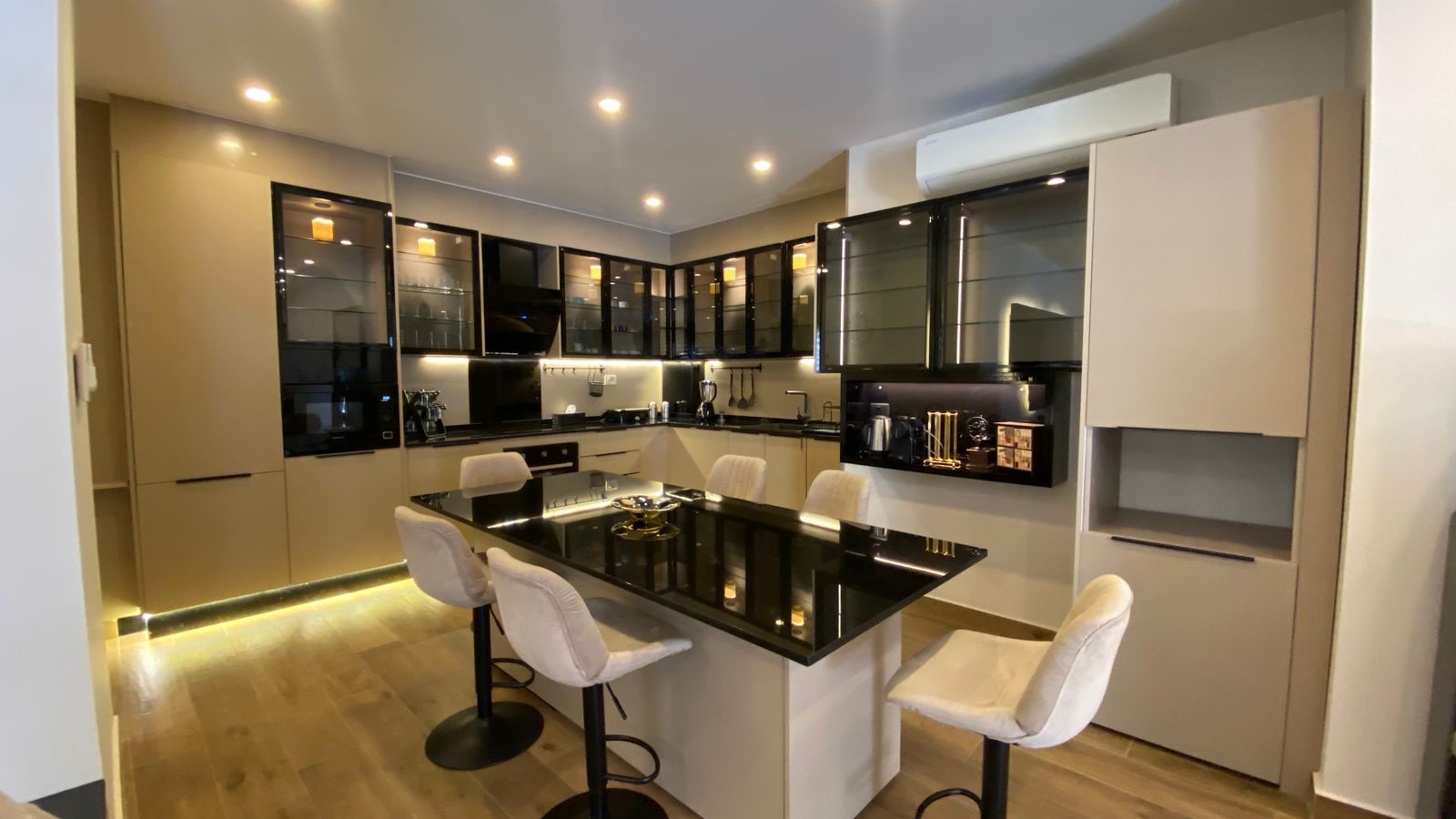 f18c60cf-a266-4cdd-819e-8d64085112a1 Modern kitchen with white and black cabinetry, a glossy black granite island, and white bar stools around it.
