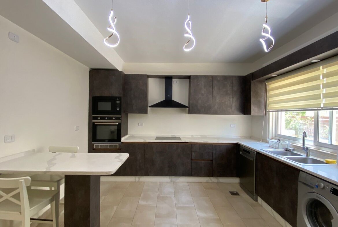 Modern L-shaped kitchen with dark brown cabinets, white countertops, and stainless appliances; island with seating.