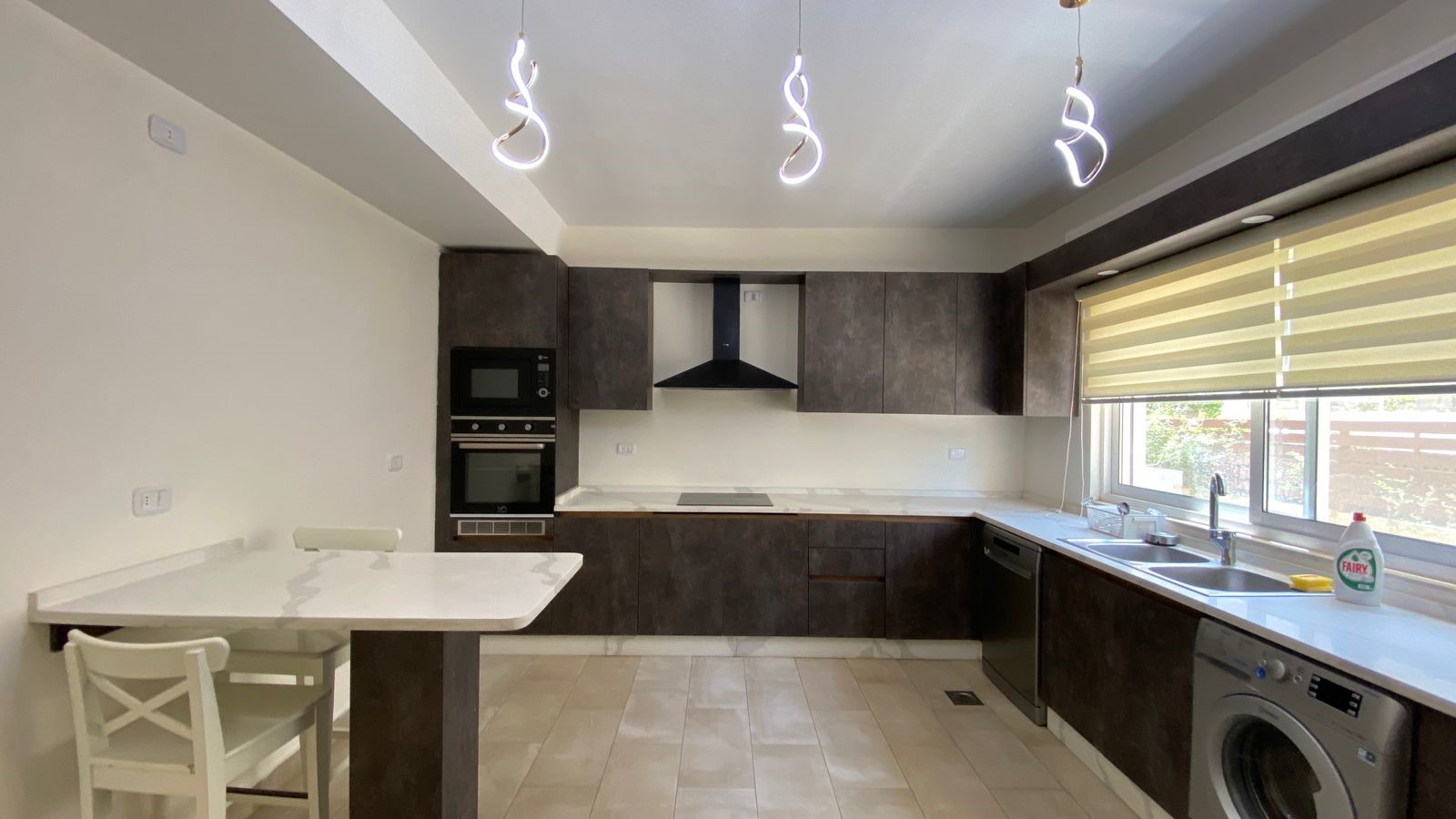 f290eaa3-37f9-4223-8c09-29723cdb0aa8 Modern L-shaped kitchen with dark brown cabinets, white countertops, and stainless appliances; island with seating.